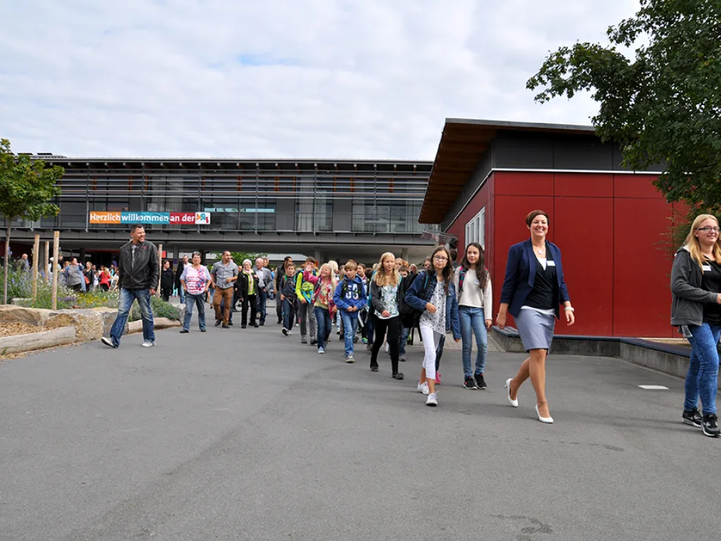 Kinder und Erwachsene gehen über den Schulhof zur Feier.